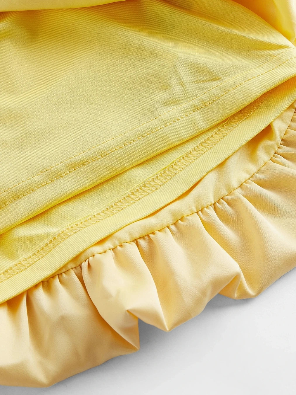 Close-up do acabamento interno e forro do Vestido Mini Ravello Amarelo Solar da BIANC, destacando a qualidade da costura e o detalhe do babado na barra.